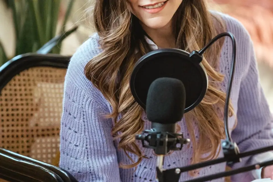 A young woman in a purple sweater sits in front of a microphone and is about to speak.